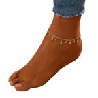 Ankle bracelet with small droplet charms on a sandy background