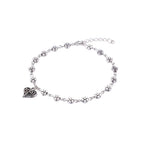 Silver anklet with heart and flower charms on a mannequin foot against a light purple background