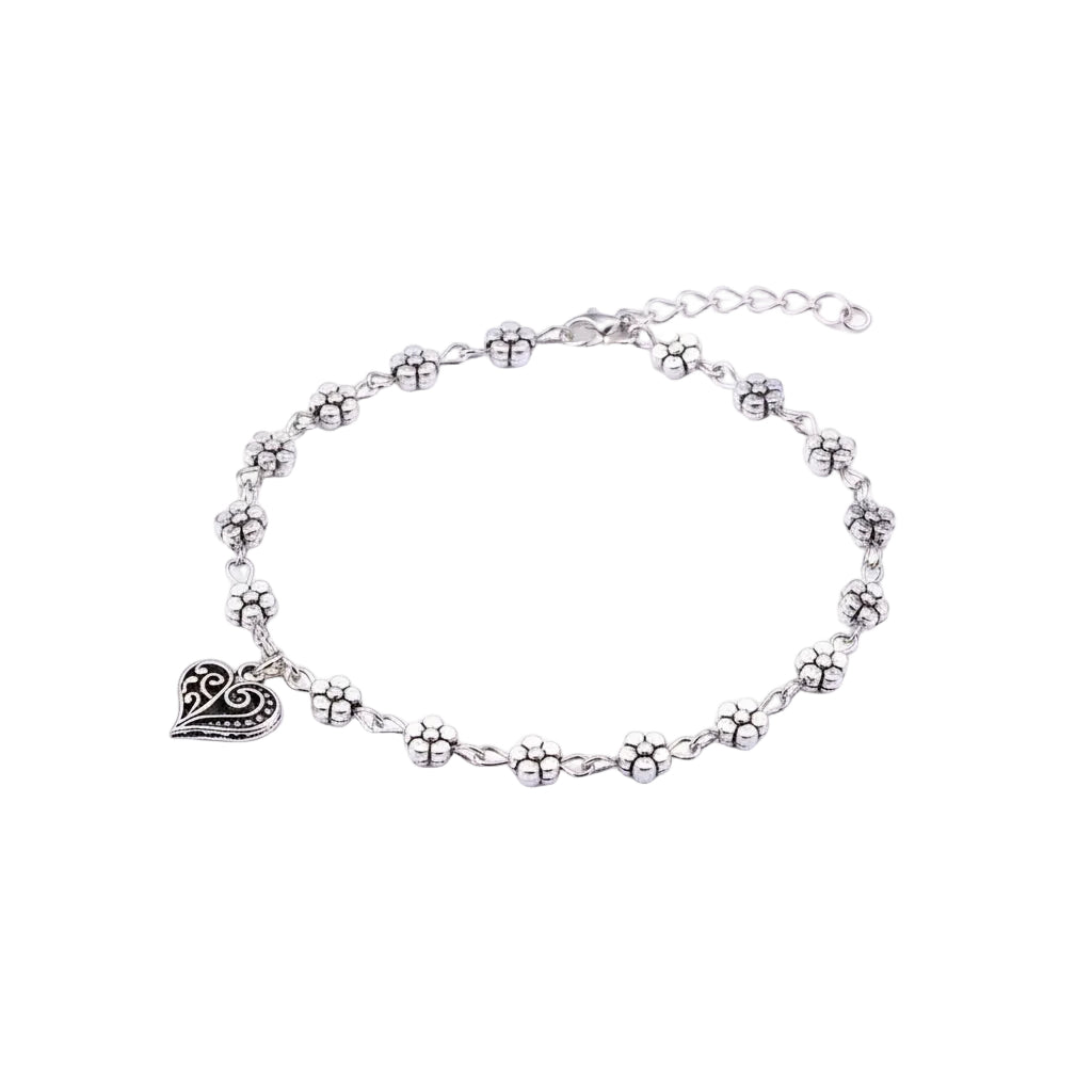 Silver anklet with heart and flower charms on a mannequin foot against a light purple background