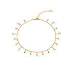Gold anklet with small droplet charms on a foot against a sandy background