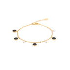 Gold anklet with black and clear beads on a foot against a white background