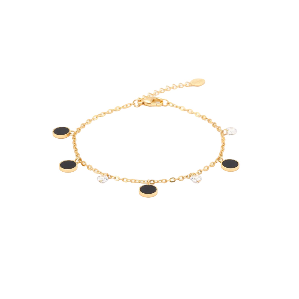 Gold anklet with black and clear beads on a foot against a white background