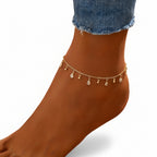 Ankle bracelet with small droplet charms on a sandy background