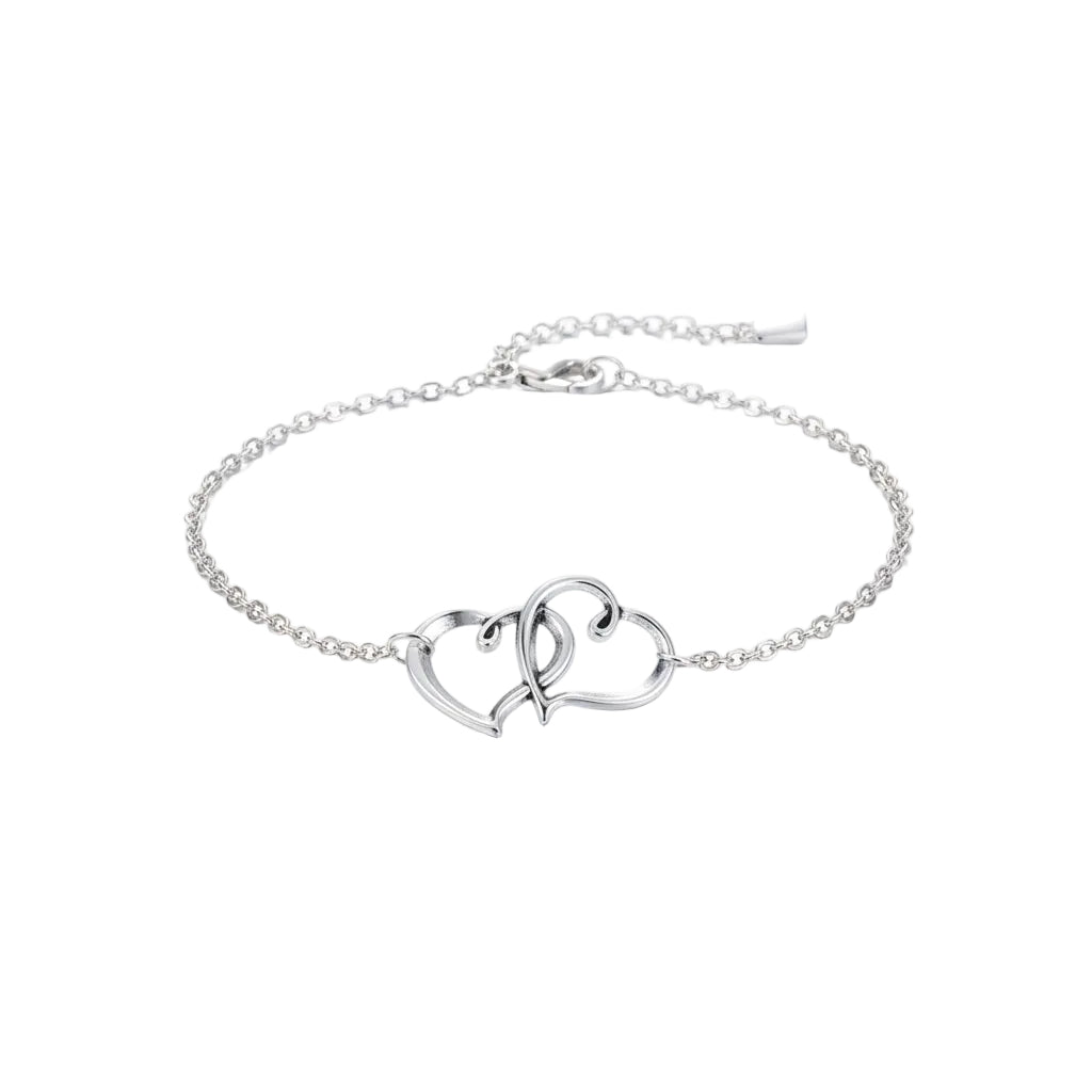Silver anklet with interlocking heart charms on a person's ankle, with flowers in the background.